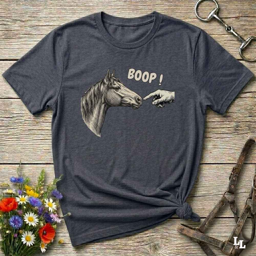 Gray t-shirt with horse graphic and 'BOOP!' text on a wooden surface with floral and equestrian accessories.