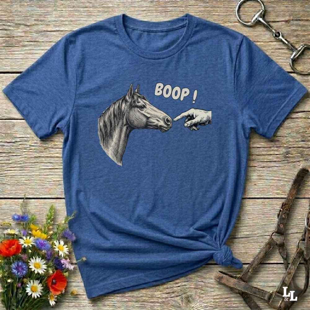 Blue t-shirt with a graphic of a horse and 'BOOP!' text on a wooden surface with floral and equestrian accessories.