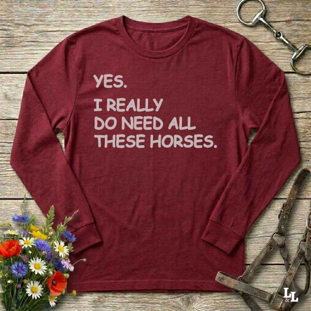 Red long-sleeve shirt with humorous text on a wooden surface with flowers and horse equipment.