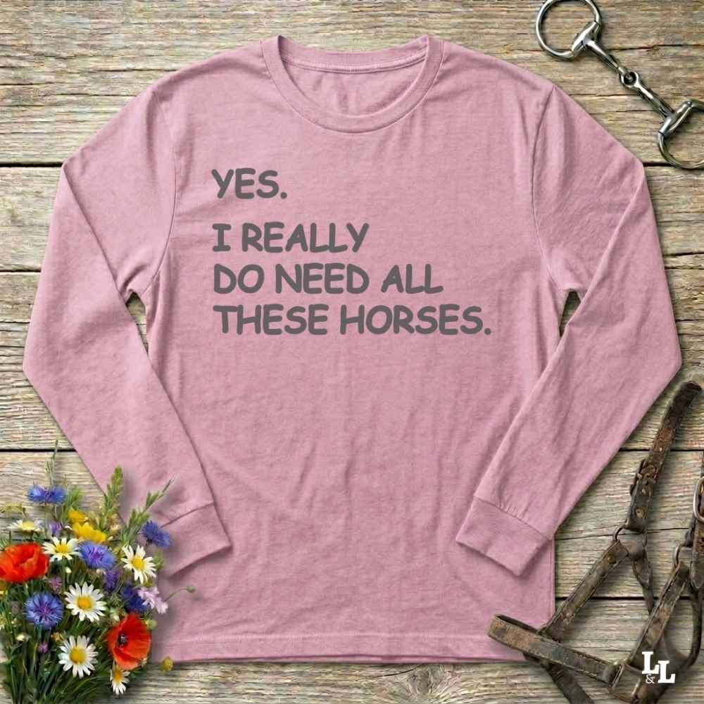 Pink long-sleeve shirt with text on a wooden surface with floral and equestrian-themed items.