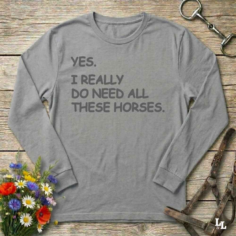 Gray long-sleeve shirt with text on a wooden surface with floral and equestrian-themed items.