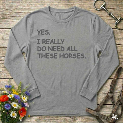 Gray long-sleeve shirt with text on a wooden surface with floral and equestrian-themed items.
