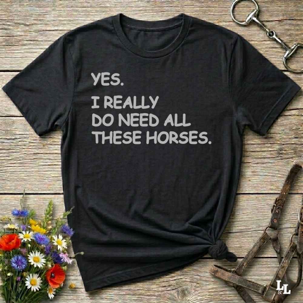Black t-shirt with humorous text on a wooden surface with equestrian-themed items.