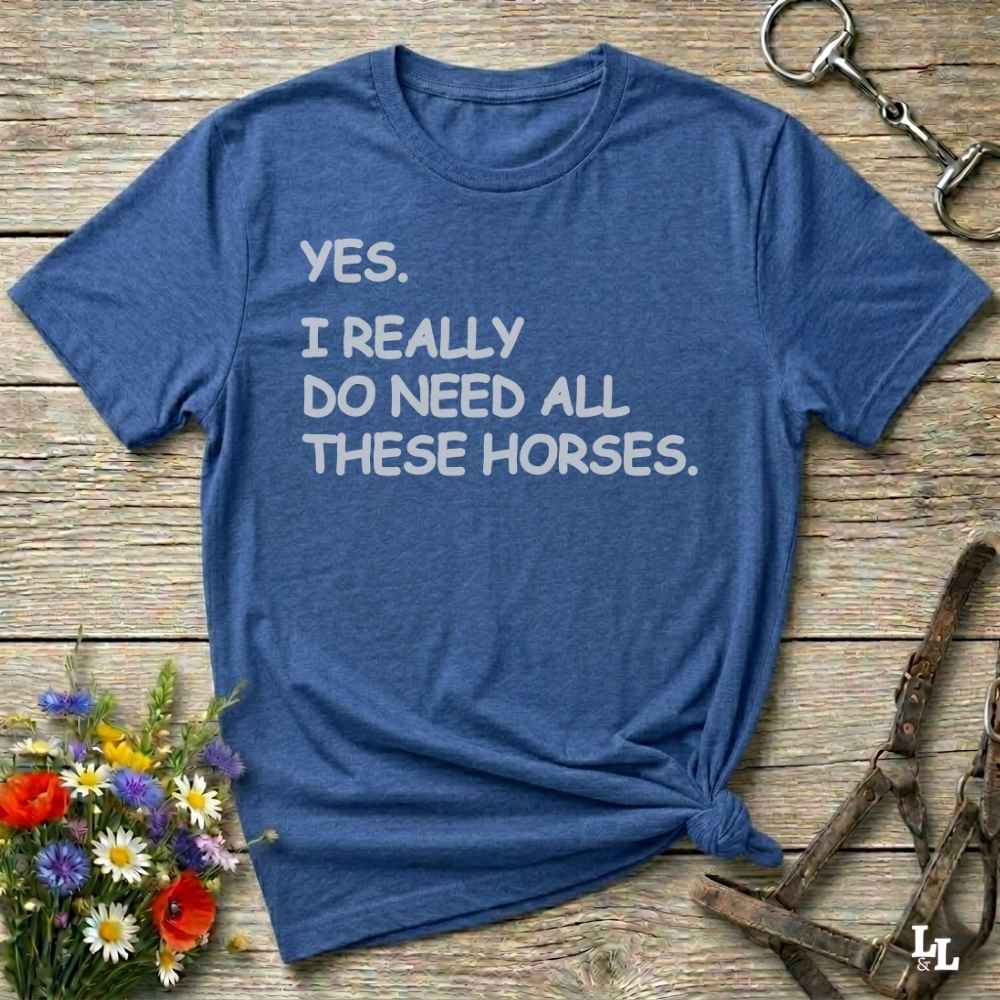 Blue t-shirt with humorous text on a wooden surface with floral and equestrian-themed accessories.
