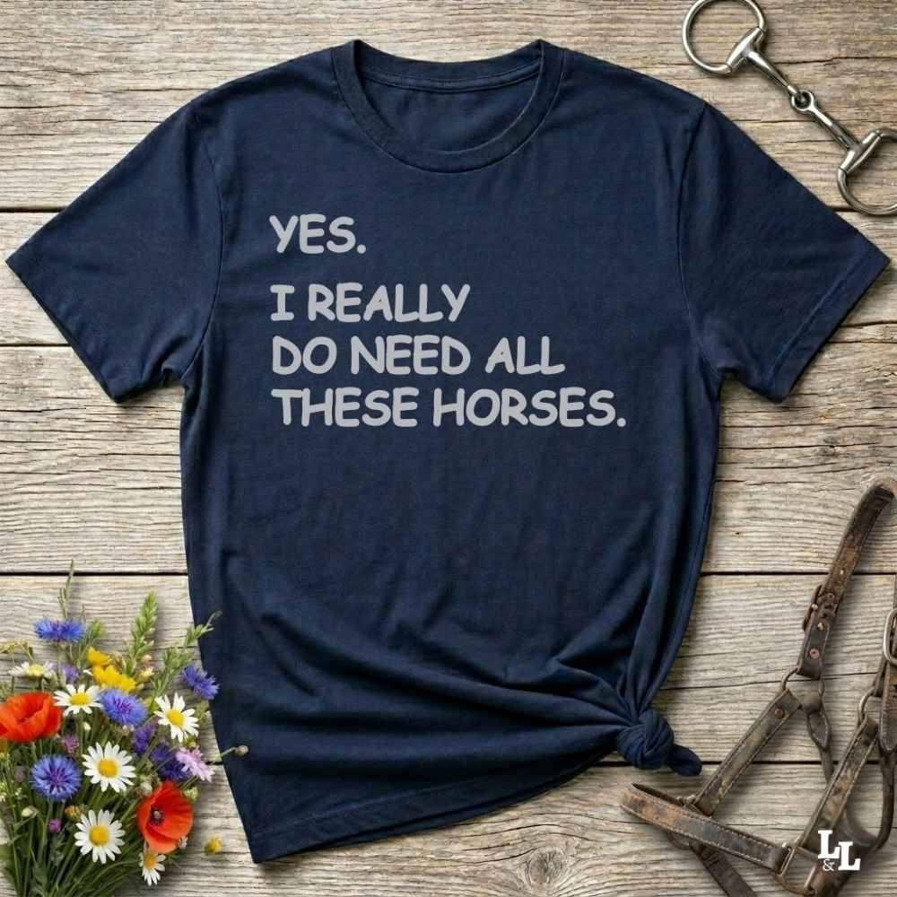 Navy blue t-shirt with humorous text on a wooden surface with floral and equestrian-themed items.