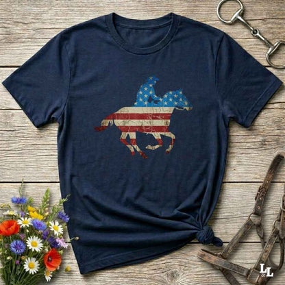 Navy blue t-shirt with American flag horse design on a wooden surface with flowers and tools.