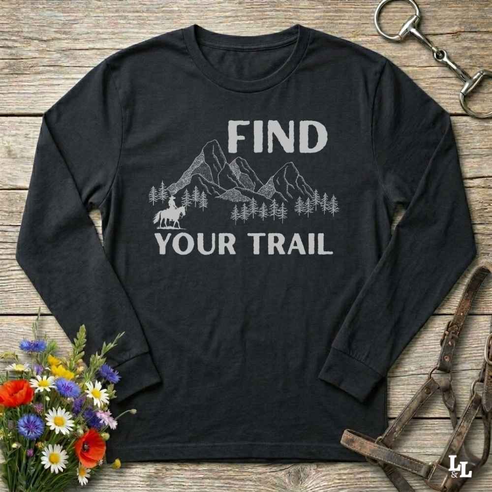 Black long-sleeve shirt with 'Find Your Trail' graphic on a wooden surface with floral and equestrian equipment.