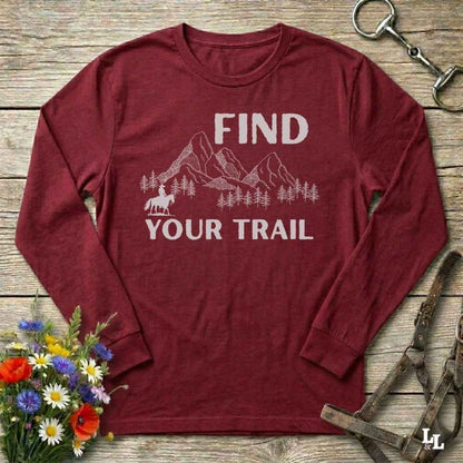 Maroon long-sleeve shirt with 'Find Your Trail' graphic on a wooden surface with flowers and horse equipment.