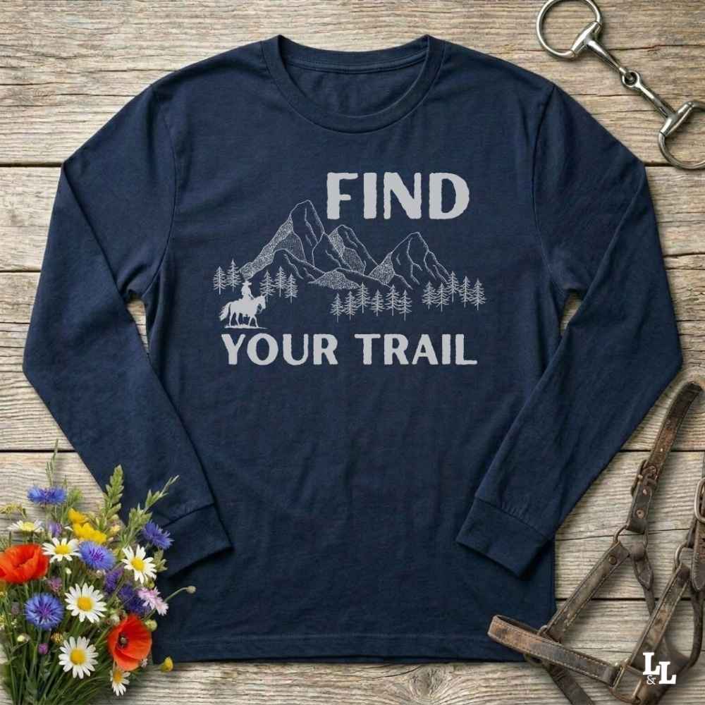 Navy blue long-sleeve shirt with 'Find Your Trail' graphic on a wooden surface with flowers and horse equipment.