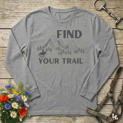 Gray long-sleeve shirt with 'Find Your Trail' graphic on a wooden background with flowers and horse equipment.