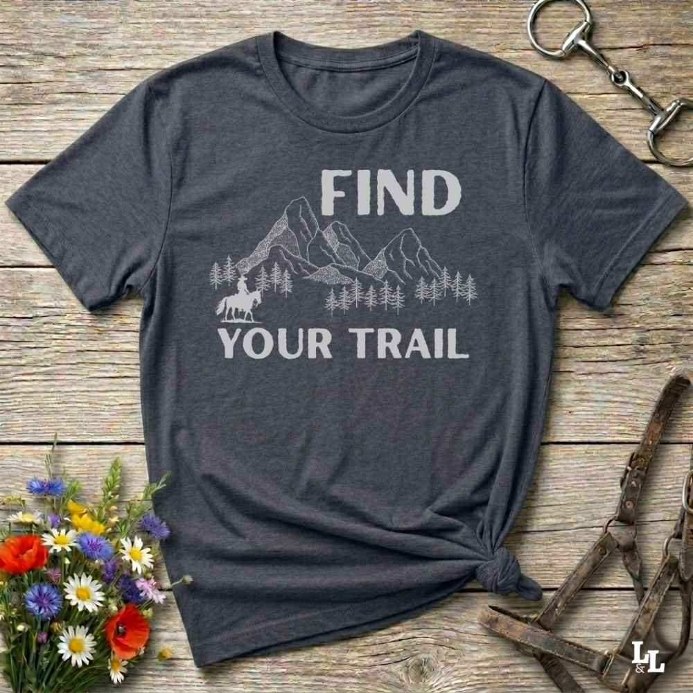 Gray t-shirt with 'Find Your Trail' graphic on a wooden surface with flowers and horse equipment.