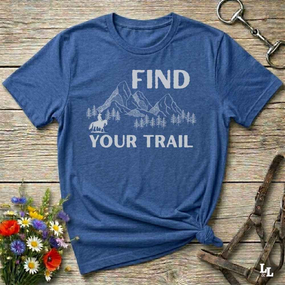 Blue t-shirt with 'Find Your Trail' text on a wooden surface with flowers and horse equipment.