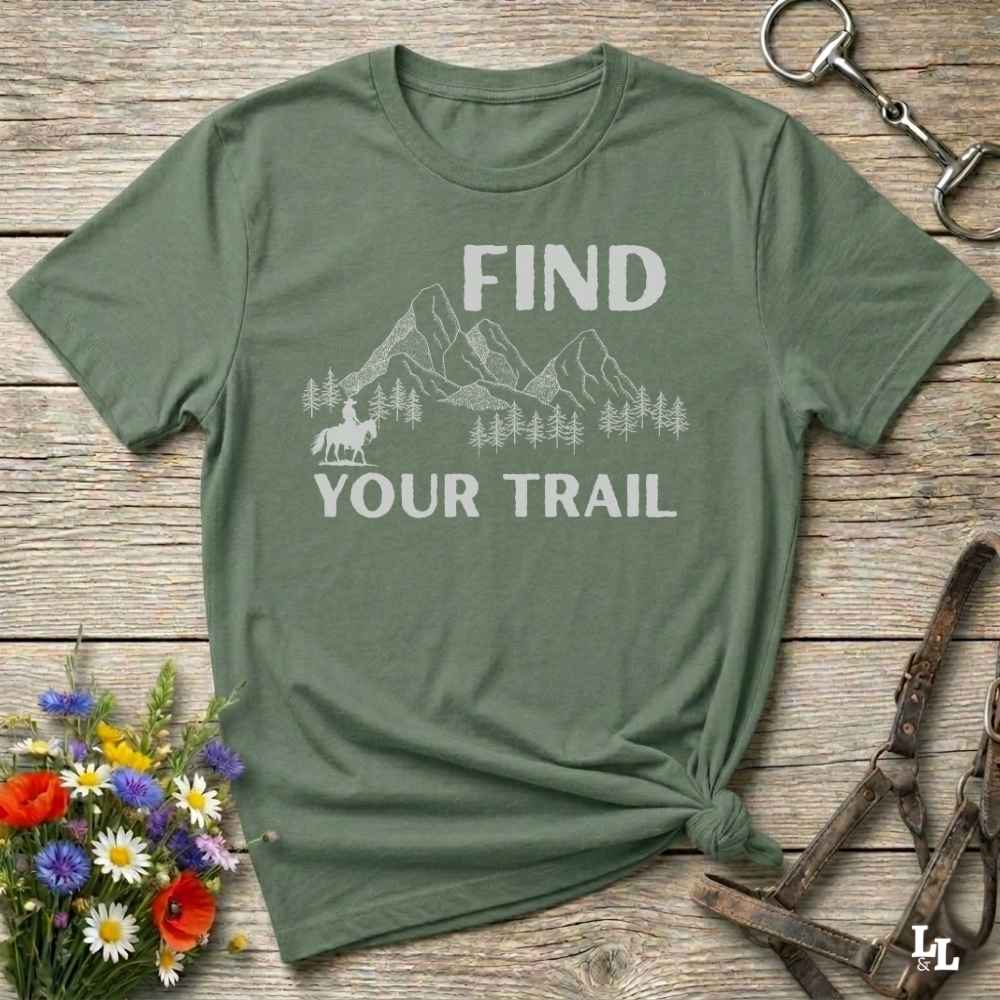 Green t-shirt with 'Find Your Trail' graphic on a wooden surface with flowers and horse equipment.