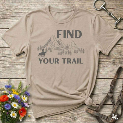 Beige t-shirt with 'Find Your Trail' graphic on a wooden surface with flowers and horse equipment.