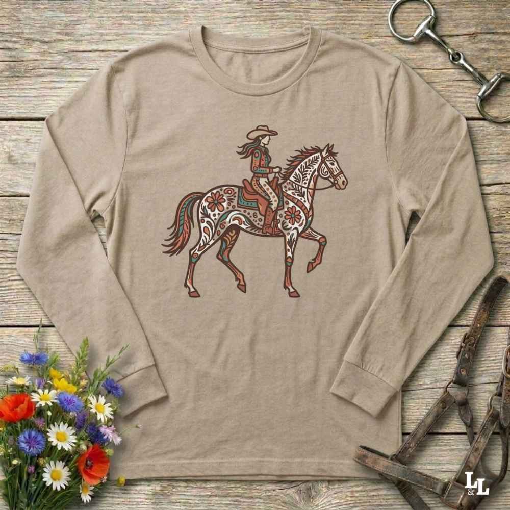 Beige long-sleeve shirt with a graphic of a woman riding a horse on a wooden surface with floral and equestrian-themed accessories.