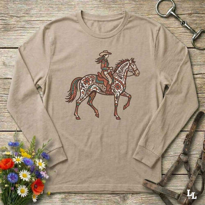 Beige long-sleeve shirt with a graphic of a woman riding a horse on a wooden surface with floral and equestrian-themed accessories.