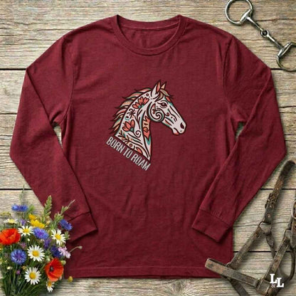 Maroon long-sleeve shirt with horse graphic and 'Born to Roam' text on a wooden surface with flowers and equestrian equipment.