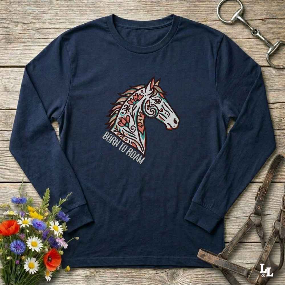 Navy blue long-sleeve shirt with a colorful horse design and 'Born to Roam' text on a wooden surface with floral and equestrian accessories.