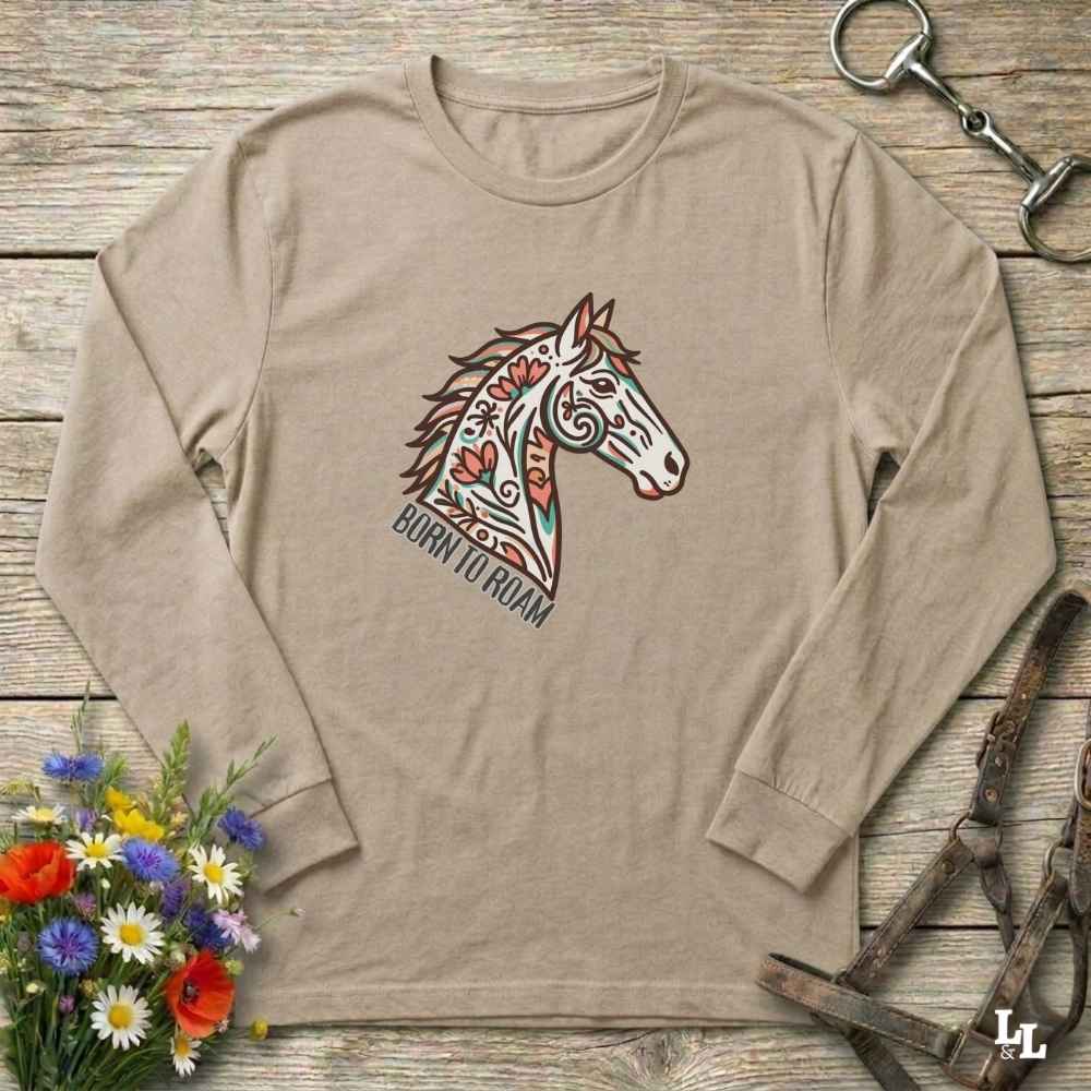 Beige long-sleeve shirt with a colorful horse graphic and text on a wooden surface with floral and equestrian-themed accessories.