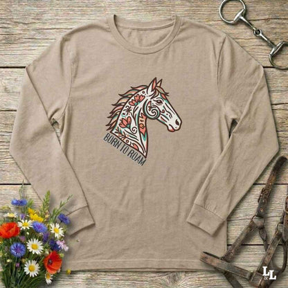 Beige long-sleeve shirt with a colorful horse graphic and text on a wooden surface with floral and equestrian-themed accessories.