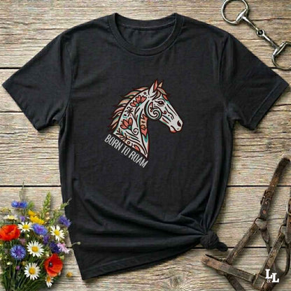 Black t-shirt with a colorful horse graphic and 'Born to Roam' text on a wooden surface with floral and equestrian-themed accessories.