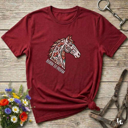 Red t-shirt with a horse graphic and 'Born to Roam' text on a wooden surface with flowers and equestrian equipment.