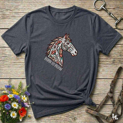 Gray t-shirt with a colorful horse graphic and 'Born to Roam' text on a wooden surface with flowers and equestrian equipment.