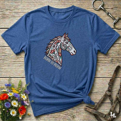 Blue t-shirt with a colorful horse graphic and text on a wooden surface with flowers and equestrian equipment.