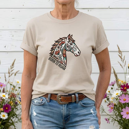 Person wearing a beige t-shirt with a horse graphic and 'Born to Roam' text, standing in front of a wooden wall with flowers.