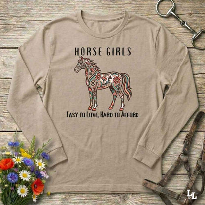 Beige long-sleeve shirt with a horse graphic and text on a wooden surface with floral and equestrian-themed accessories.