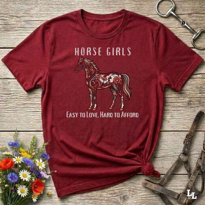 Red t-shirt with horse graphic and text on a wooden surface with floral and equestrian-themed accessories.