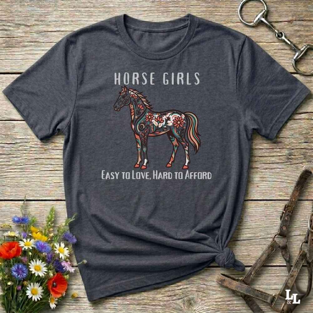 Gray t-shirt with horse graphic and text on a wooden surface with floral and equestrian accessories.