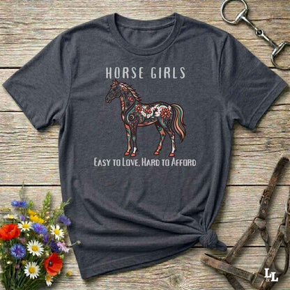 Gray t-shirt with horse graphic and text on a wooden surface with floral and equestrian accessories.
