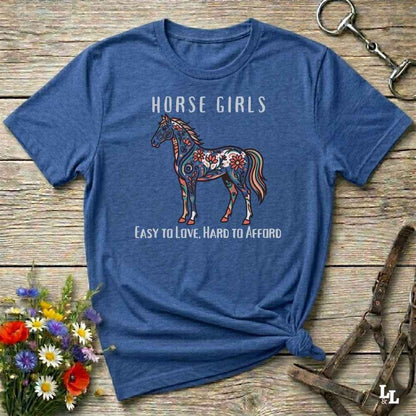 Blue t-shirt with a horse graphic and text on a wooden surface with floral and equestrian accessories.