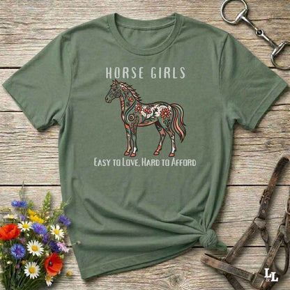 Green t-shirt with horse graphic and text on a wooden surface with floral and equestrian-themed accessories.