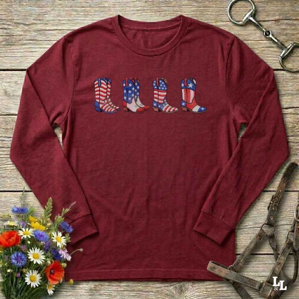 Maroon long-sleeve shirt with American flag cowboy boot design on a wooden surface with floral and equestrian elements.