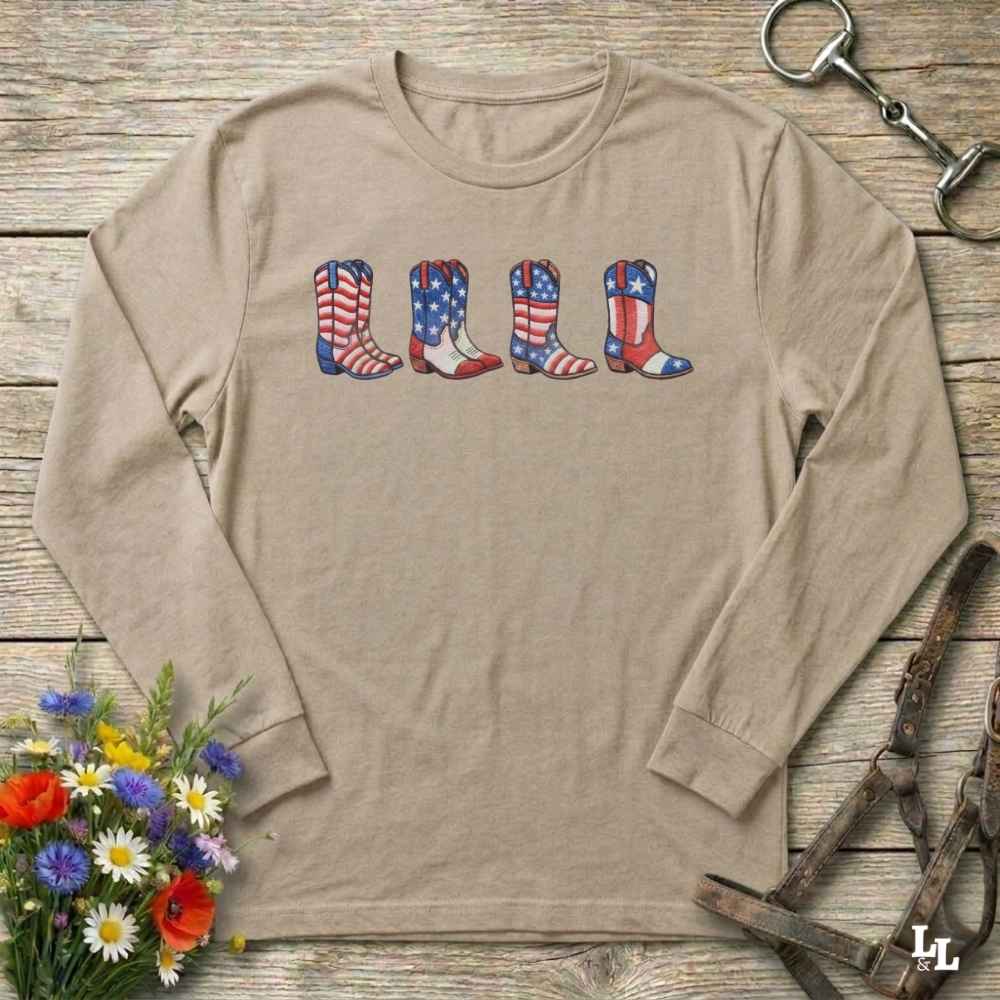 Beige long-sleeve shirt with American flag cowboy boots design on a wooden surface with floral and equestrian elements.