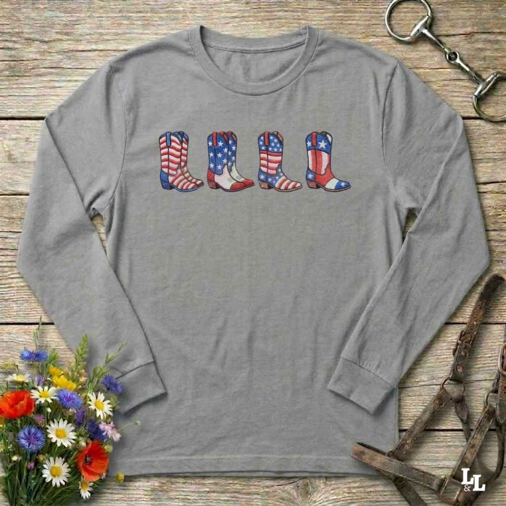 Gray long-sleeve shirt with American flag cowboy boots design on a wooden surface with flowers and horse reins.