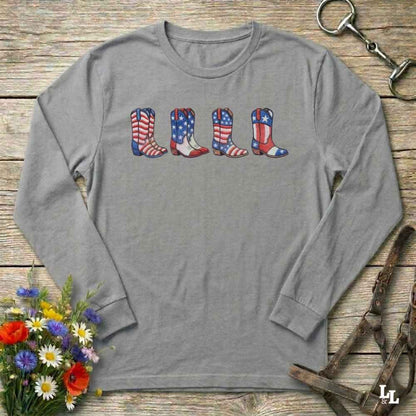 Gray long-sleeve shirt with American flag cowboy boots design on a wooden surface with flowers and horse reins.