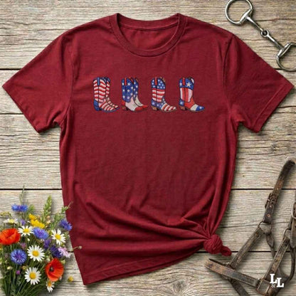 Red t-shirt with American flag cowboy boot design on a wooden surface with flowers and tools.