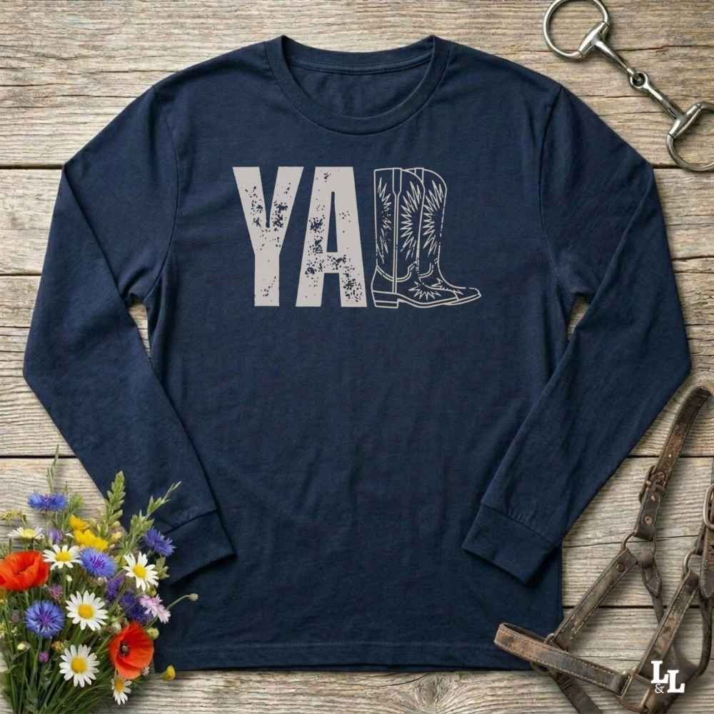 navy blue  long-sleeve shirt with 'YALL' and boot design on a wooden barn floor with flowers and horse equipment.