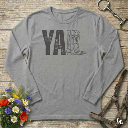gray  long-sleeve shirt with 'YALL' and boot design on a wooden barn floor with flowers and horse equipment.