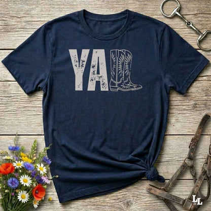 navy blue t-shirt lying flat on wooden barn floor, with graphic design saying "YALL" with the l's being cowboy boots.