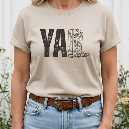 t-shirt lying flat on wooden barn floor, with graphic design saying "YALL" with the l's being cowboy boots.