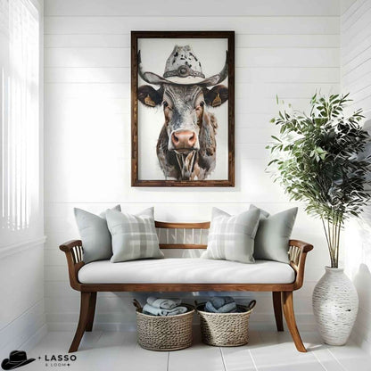 Framed picture of a cow wearing a hat above a wooden bench with cushions in a room. Longhorn Cow Poster.