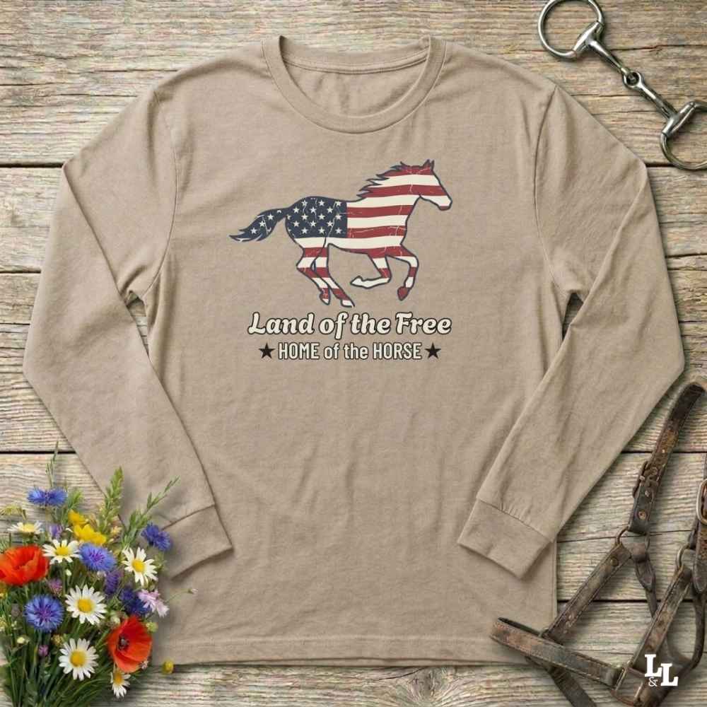 Beige long-sleeve shirt with American flag horse design on a wooden surface with floral and equestrian elements.