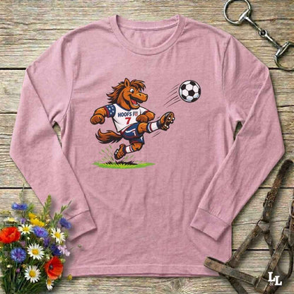 Pink long-sleeve shirt with a cartoon horse kicking a soccer ball on a wooden surface with flowers and a horse bridle.