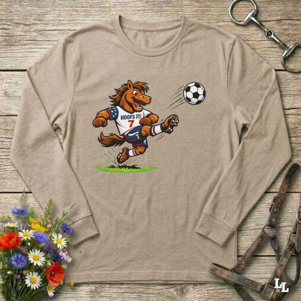beige  long-sleeve shirt with a cartoon horse kicking a soccer ball on a wooden surface with flowers and a horse bridle.