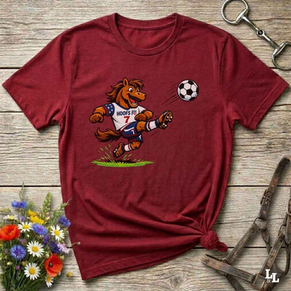 red t-shirt with a cartoon horse kicking a soccer ball on a wooden surface with flowers and horse halter and bit.