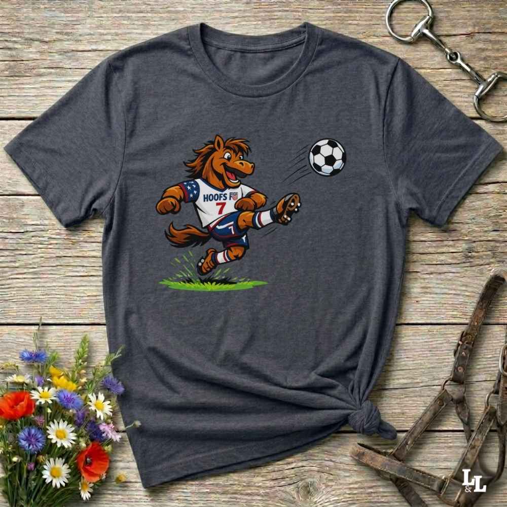 gray t-shirt with a cartoon horse kicking a soccer ball on a wooden surface with flowers and horse halter and bit.